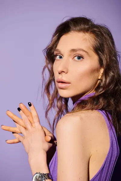 Stylish young woman in vibrant purple dress elegantly holds her hand up against a purple background. — Stock Photo