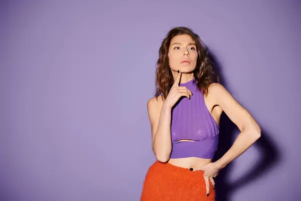 A stylish young woman showcasing a vibrant orange skirt and a purple top against a bold purple backdrop. — Stock Photo