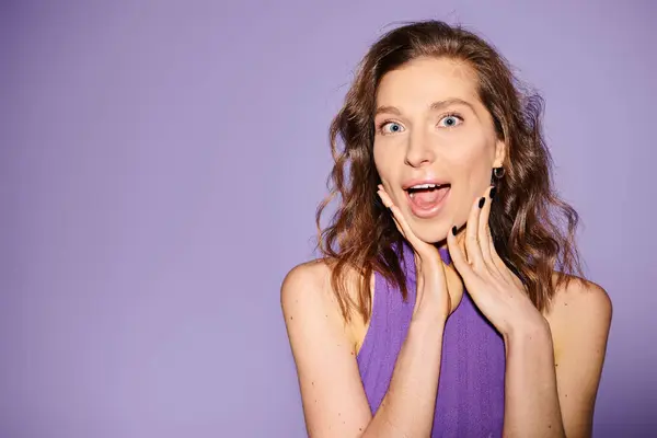A stylish young woman in a purple top is making a funny face against a vibrant purple background. — Stock Photo