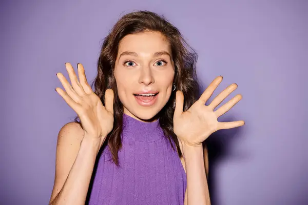 Stylish young woman in a purple top energetically holds her hands up against a vibrant purple background. — Stock Photo