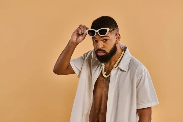 Un homme élégant portant des lunettes de soleil et une chemise, respirant confiance et charme tout en frappant une pose. — Photo de stock