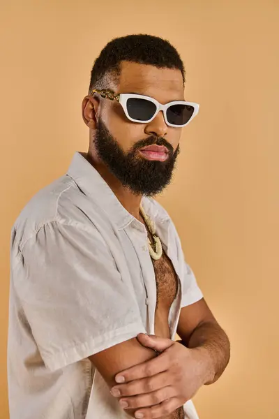 Un hombre con barba llena y gafas de sol está de pie con confianza, exudando un sentido de misterio y estilo. - foto de stock