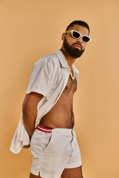 Um homem na moda em shorts brancos e óculos de sol elegantes está confiantemente posando para uma imagem, exalando elegância e carisma sob o brilho quente sóis. — Fotografia de Stock