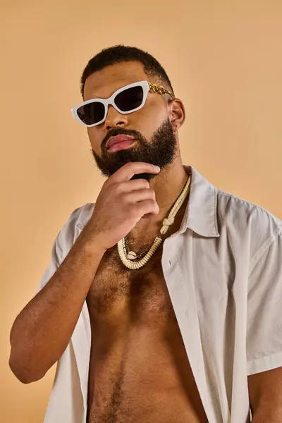 Мужчина с бородой носит солнцезащитные очки и ожерелье, излучая прохладное и уверенное поведение, когда он стоит на ногах. — стоковое фото