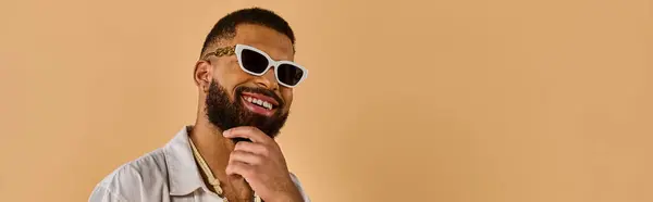 Человек с бородой и прохладными солнцезащитными очками, излучающий уверенность и стиль, выделяющийся в толпе своим уникальным внешним видом. — стоковое фото