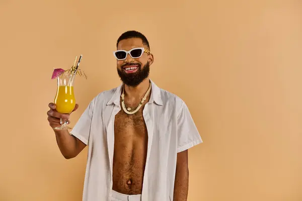 Um homem elegante usando óculos de sol segura um copo de suco, exalando relaxamento e prazer sob os raios de sóis. — Fotografia de Stock