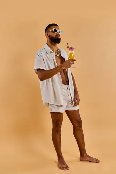 Un hombre con estilo en una camisa blanca y pantalones cortos disfruta de una bebida refrescante en un entorno sereno, exudando relajación y satisfacción. - foto de stock