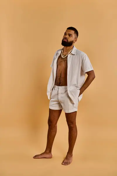 Um homem está confiante em uma camisa branca e shorts, exalando uma aura casual, mas elegante. Ele olha para a distância, irradiando uma sensação de confiança tranquila e facilidade. — Fotografia de Stock