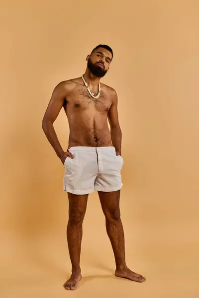 A man with no shirt standing confidently in front of a tan background, showcasing his muscular physique and sense of self-assurance. — Stock Photo
