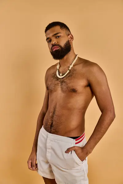Un uomo con la barba piena sta in piedi con fiducia, indossando pantaloncini bianchi. La sua barba aggiunge un tocco robusto al suo abbigliamento rilassato e casual. — Foto stock