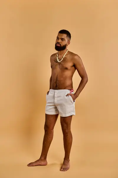 Un uomo vestito di pantaloncini bianchi si trova con fiducia davanti a un muro abbronzato, trasudando un senso di stile e raffinatezza in un ambiente semplice ma sorprendente.. — Foto stock