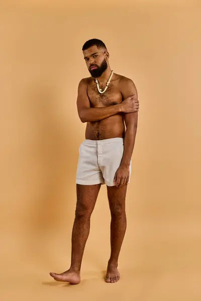 Um homem usando shorts brancos fica com uma postura confiante, cruzando os braços com uma expressão serena em seu rosto.. — Fotografia de Stock