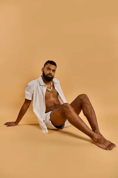 A man dressed in a shirt and shorts sits on the ground, deep in thought with a serene expression on his face. — Stock Photo