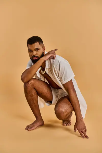 Un hombre gentilmente se arrodilla con su mano descansando confiadamente sobre su cadera, mostrando aplomo y seguridad en sí mismo. - foto de stock