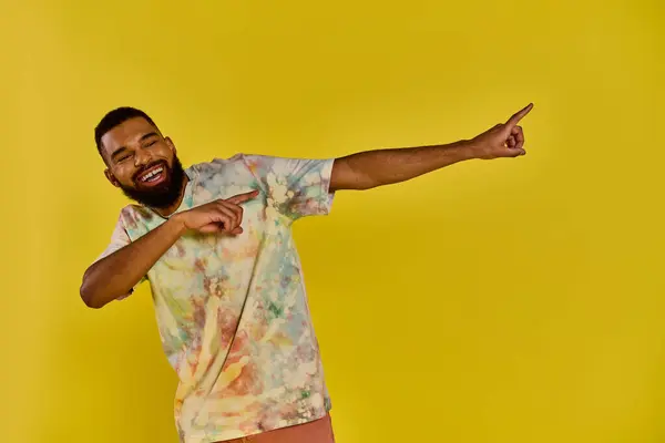A man wearing a vibrant tie dye shirt points animatedly at something out of frame, his colorful attire standing out against a neutral backdrop. — Stock Photo