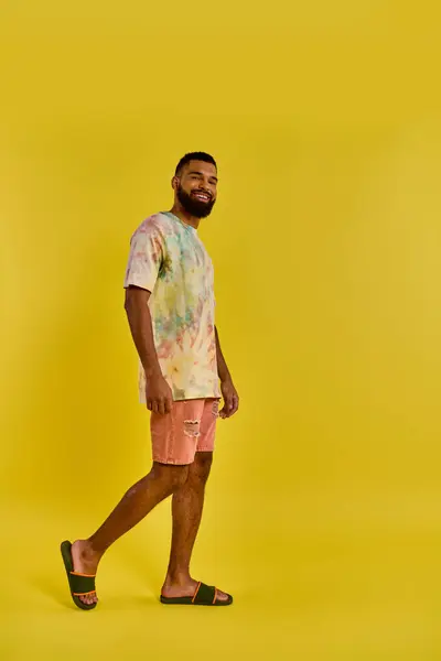 Un uomo che indossa una camicia colorata tinta cravatta e pantaloncini abbinati si erge con fiducia, mostrando il suo stile unico e vibrante in un ambiente casual. — Foto stock