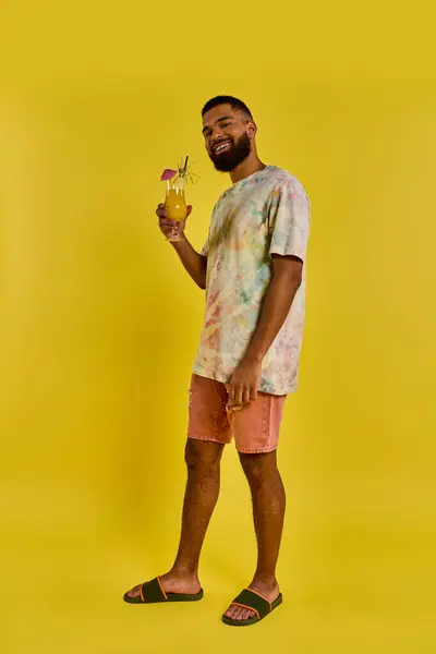 Un hombre se para confiadamente frente a un vibrante telón de fondo amarillo, sosteniendo una bebida delicadamente en su mano mientras mira hacia adelante. - foto de stock