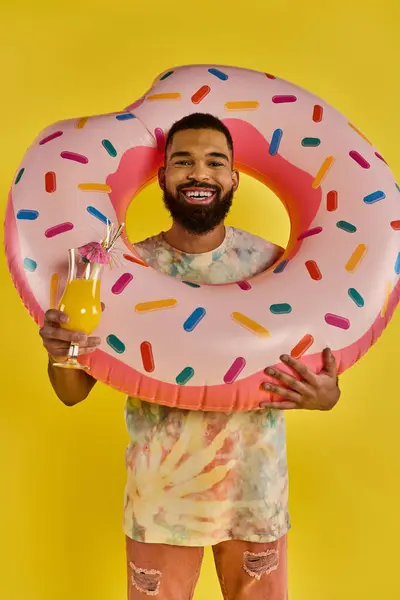 Ein Mann hält freudig einen riesigen Donut in der einen Hand und ein Glas Bier in der anderen und schwelgt in dem leckeren und genussvollen Moment. — Stockfoto
