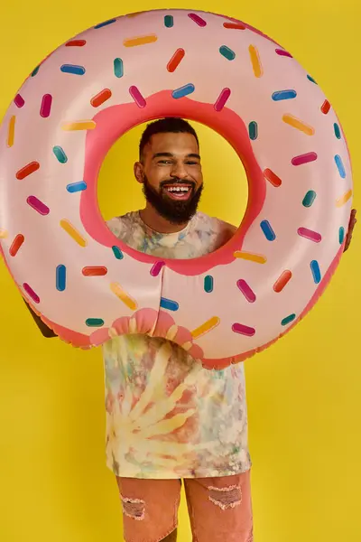 Un hombre se esconde juguetonamente detrás de un enorme donut, mostrando su lado caprichoso y humorístico mientras disfruta de un sabroso manjar.. - foto de stock