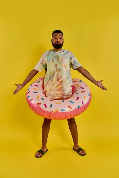 Ein stilvoller Mann im Krawattenhemd hält einen bunten Donut-Wagen, der inmitten einer sommerlichen Szene mit einer skurrilen Note steht.. — Stockfoto