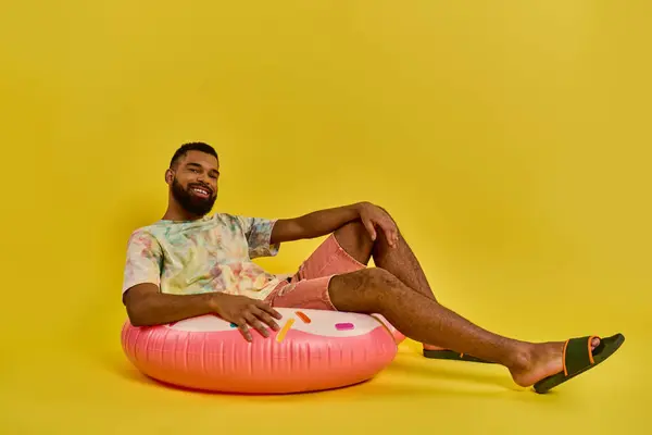A man sits gracefully on a pink inflatable object, looking peaceful and content as he enjoys a moment of relaxation on the soft surface. — Stock Photo