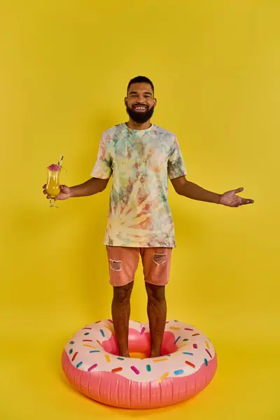 Ein Mann balanciert selbstbewusst auf einem riesigen Donut, trinkt in der Hand, in einer surrealen und skurrilen Szene. — Stockfoto
