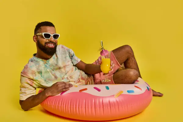 A man in a relaxed posture is sitting on the vibrant pink doughnut float, exuding a sense of calmness and leisure on the water. — Stock Photo
