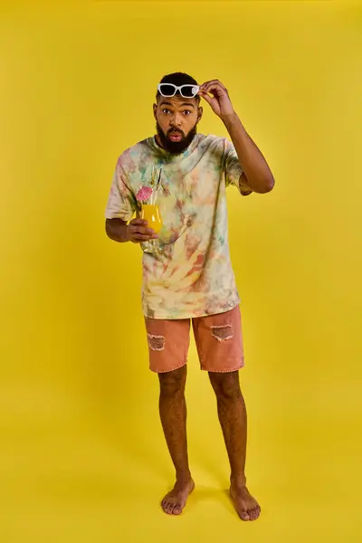 A stylish man in a vibrant tie dye shirt is holding a refreshing drink in his hand, exuding a carefree and relaxed vibe. — Stock Photo
