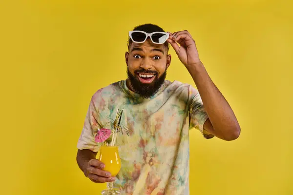 A man wearing a colorful tie-dye shirt is holding a drink in his hand, standing in a relaxed pose. — Stock Photo