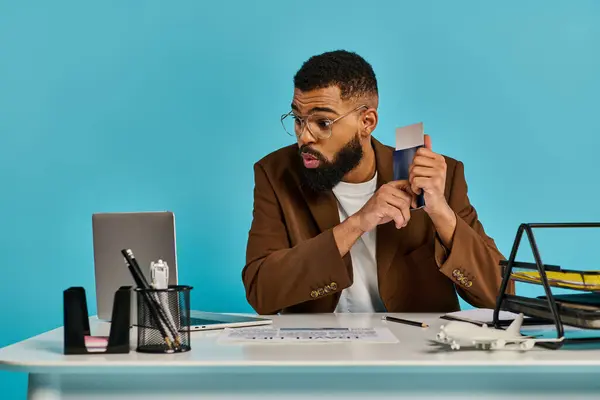 Un hombre enfocado sentado en un escritorio, profundamente pensado, sosteniendo una tarjeta de crédito en su mano, contemplando una compra o decisión financiera. - foto de stock