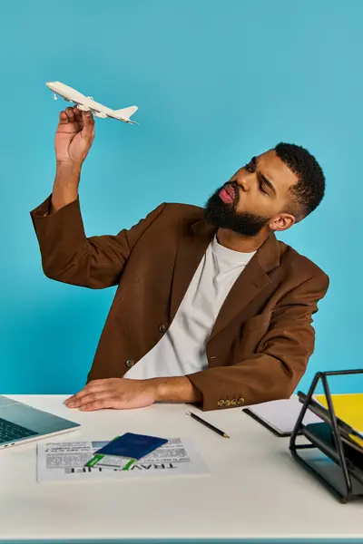 Un hombre se sienta en un escritorio, enfocado en una pantalla de computadora portátil mientras un avión modelo se sienta a su lado, mostrando su pasión por la aviación. - foto de stock