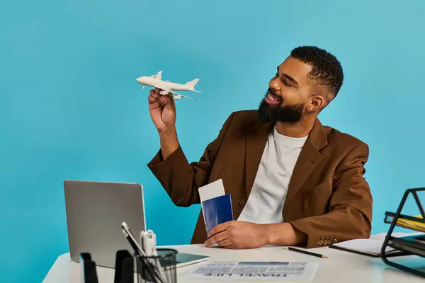 Un uomo si siede ad una scrivania, con in mano un modellino di aeroplano, profondamente pensieroso. Esamina attentamente e lavora sugli intricati dettagli dei piccoli aerei. — Foto stock