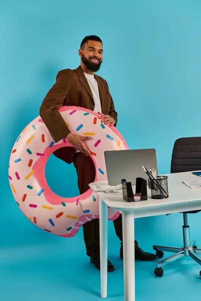 Ein Mann sitzt an einem Schreibtisch und starrt auf einen riesigen Donut vor sich. Der Donut ist überlebensgroß, verlockend und surreal. — Stockfoto