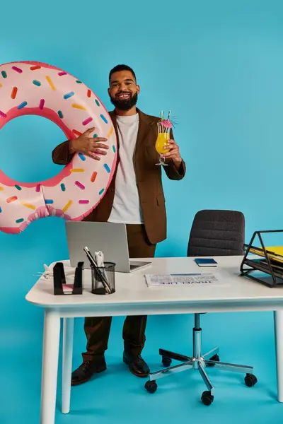 Ein Mann mit freudigem Gesichtsausdruck hält in der einen Hand einen riesigen, köstlichen Donut, während er in der anderen ein erfrischendes Getränk balanciert. — Stockfoto