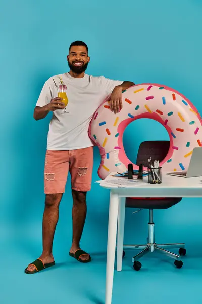 Чоловік стоїть поруч зі столом, дивлячись схвильований, з гігантським пончиком, розміщеним на ньому. — стокове фото