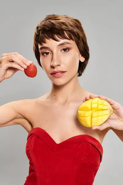 Una joven con un vestido rojo sosteniendo una pieza de fruta. - foto de stock