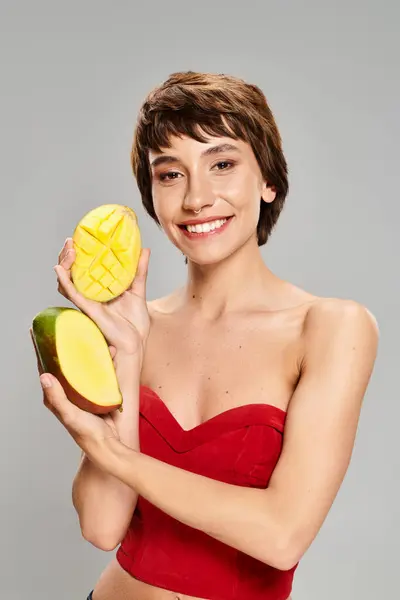 Молода жінка в червоній верхній частині тримає манго. — стокове фото