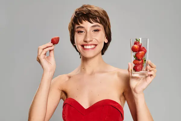 A young woman in a red dress delicately holds a glass of strawberries. — Stock Photo