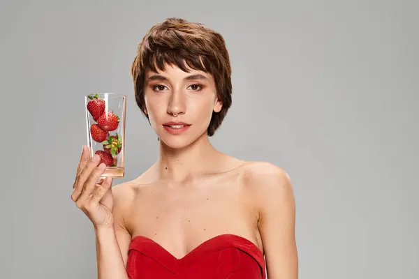 Mujer joven en vestido rojo sostiene vaso de fresas. - foto de stock