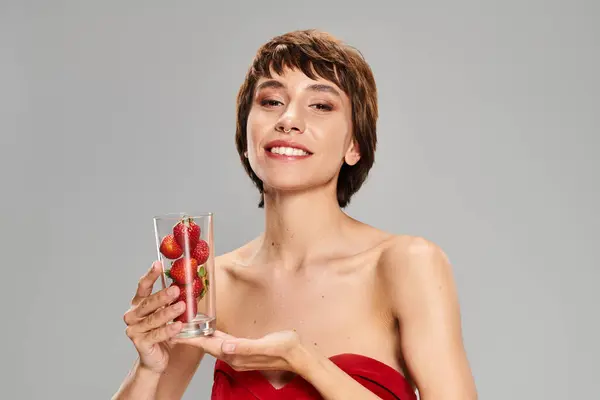 Une jeune femme gracieuse dans une robe rouge tenant un verre de fruits sur un fond vibrant. — Photo de stock