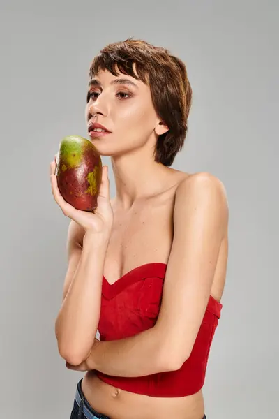 Молода жінка в червоній верхівці тримає стиглий манго в яскравій обстановці. — стокове фото