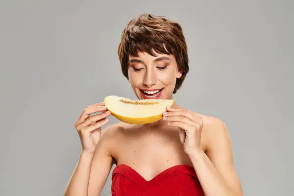 Una donna vestita di rosso mangia delicatamente un frutto. — Foto stock