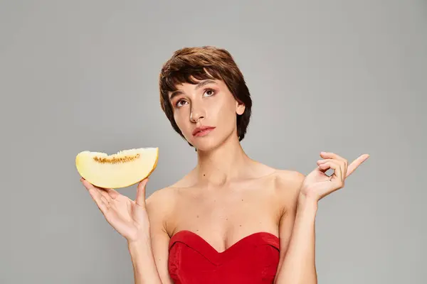 Donna elegante in un vestito rosso regge con grazia un pezzo di frutta. — Foto stock