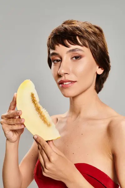 Una joven cautivadora con un vestido rojo brillante posando con un mango maduro. — Stock Photo