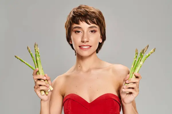 Stylish woman in red dress gracefully holding asparagus. — Stock Photo