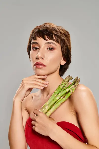 A young woman in a red dress gracefully holds a bunch of asparagus. — Stock Photo