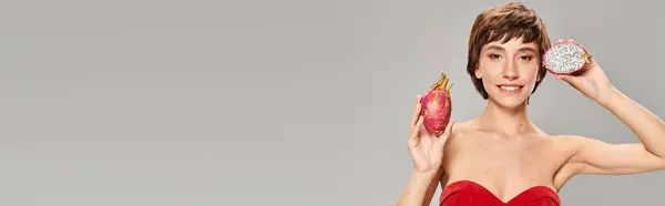 A stylish young woman in a red dress holding a dragon fruit. — Stock Photo