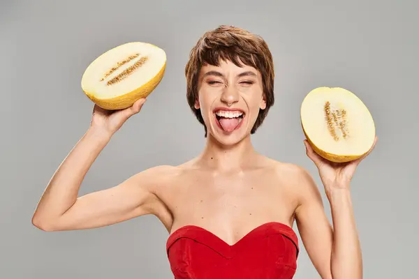 A young woman in a striking red dress holding two pieces of fruit. — Stock Photo