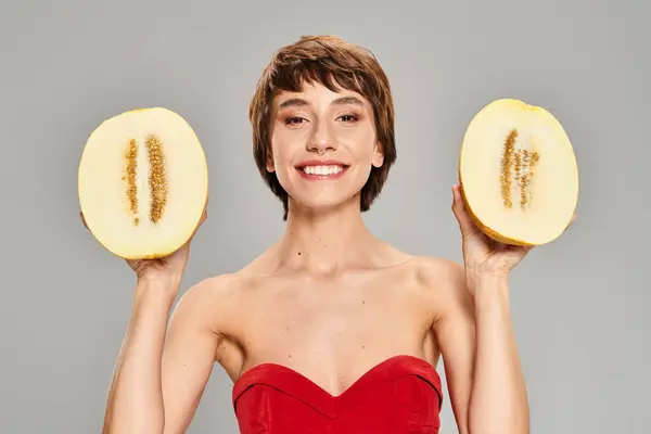 Elegant woman in red dress holds two melon slices. — Stock Photo