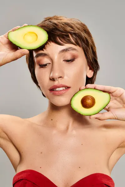 Young woman playfully holds an avocado up to her face against a vibrant backdrop. — Stock Photo